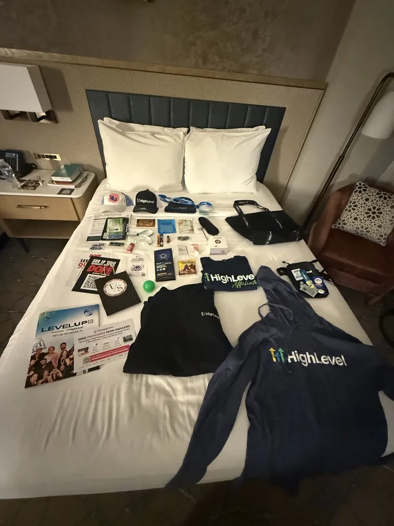 HighLevel LevelUp 2026 conference swag laid out on a hotel bed, including a hoodie, shirts, hat, and program